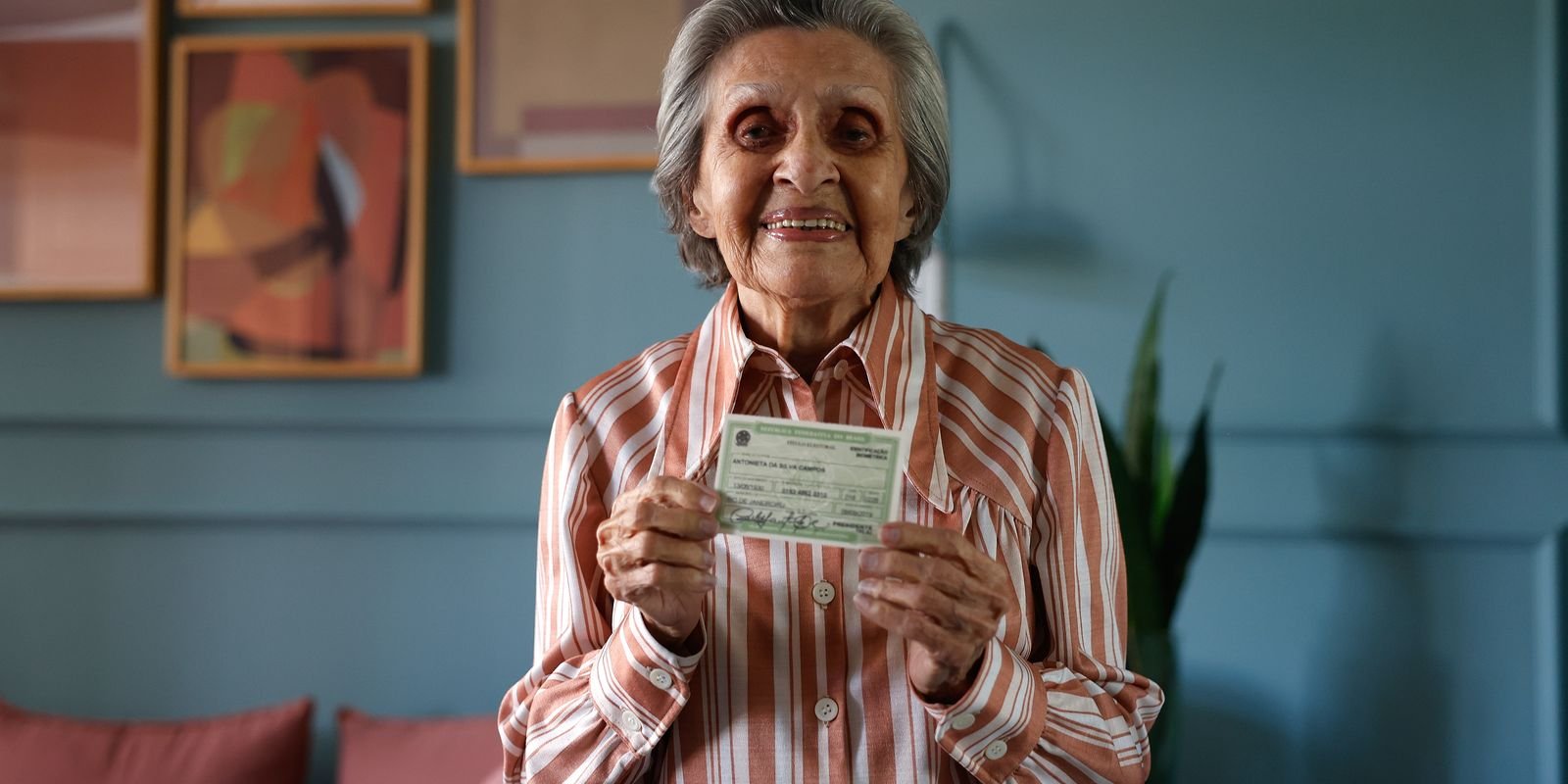 Eleitora idosa sorri e mostra o título de eleitor