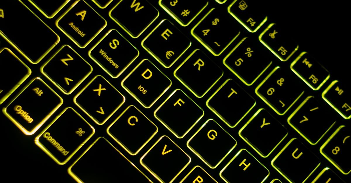 Teclado de computador retroiluminado em ambiente escuro, com brilho amarelo esverdeado nas teclas