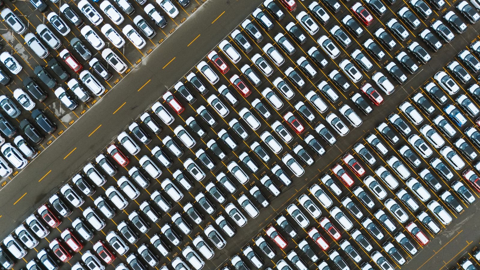 Vista aérea de fileiras de carros estacionados lado a lado em um pátio asfaltado