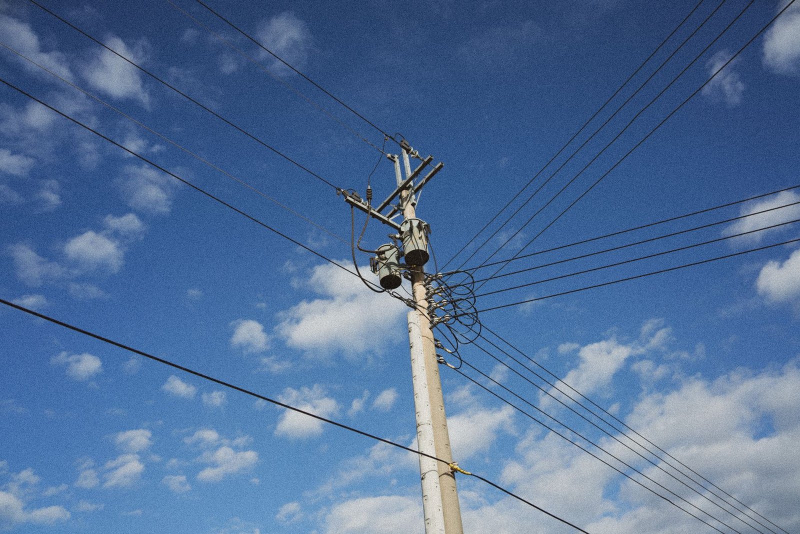 Poste de energia elétrica com transformador e fios contra o céu azul com nuvens