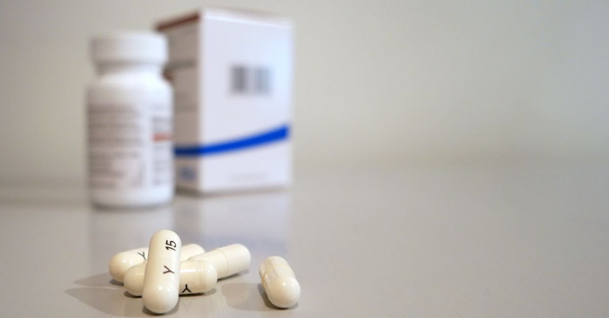 Cápsulas brancas sobre superfície clara, ao lado de frasco e caixa de medicamento