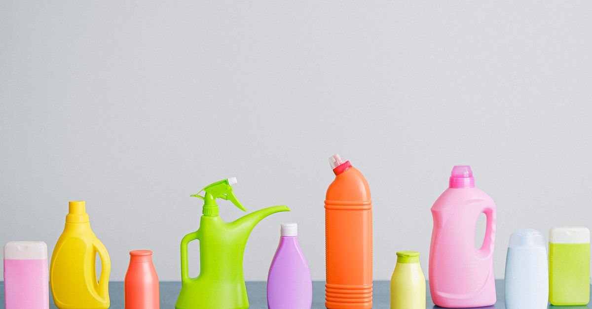 Frascos plásticos coloridos de produtos de limpeza enfileirados sobre superfície clara