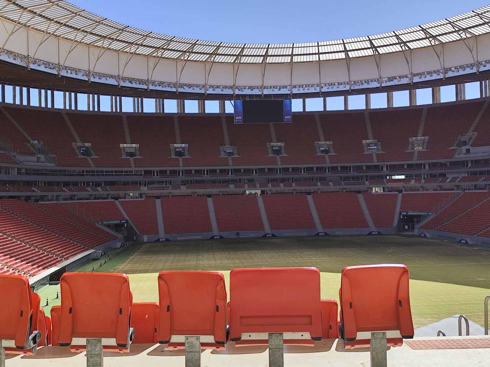 Interior da Arena BRB Mané Garrincha, com arquibancadas vermelhas vazias, telão e gramado, foto de arquivo