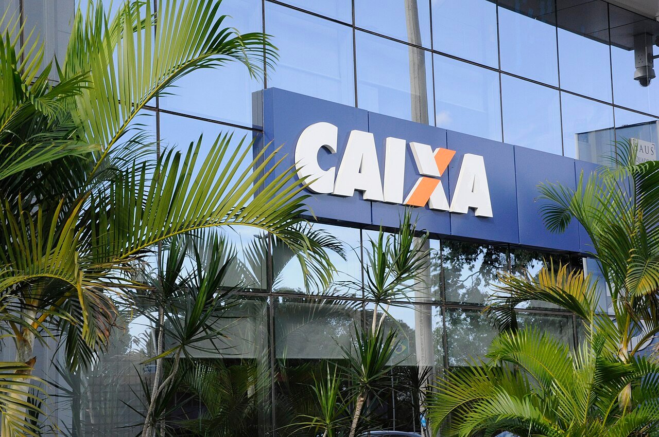 Fachada de agência da Caixa Econômica Federal cercada por palmeiras