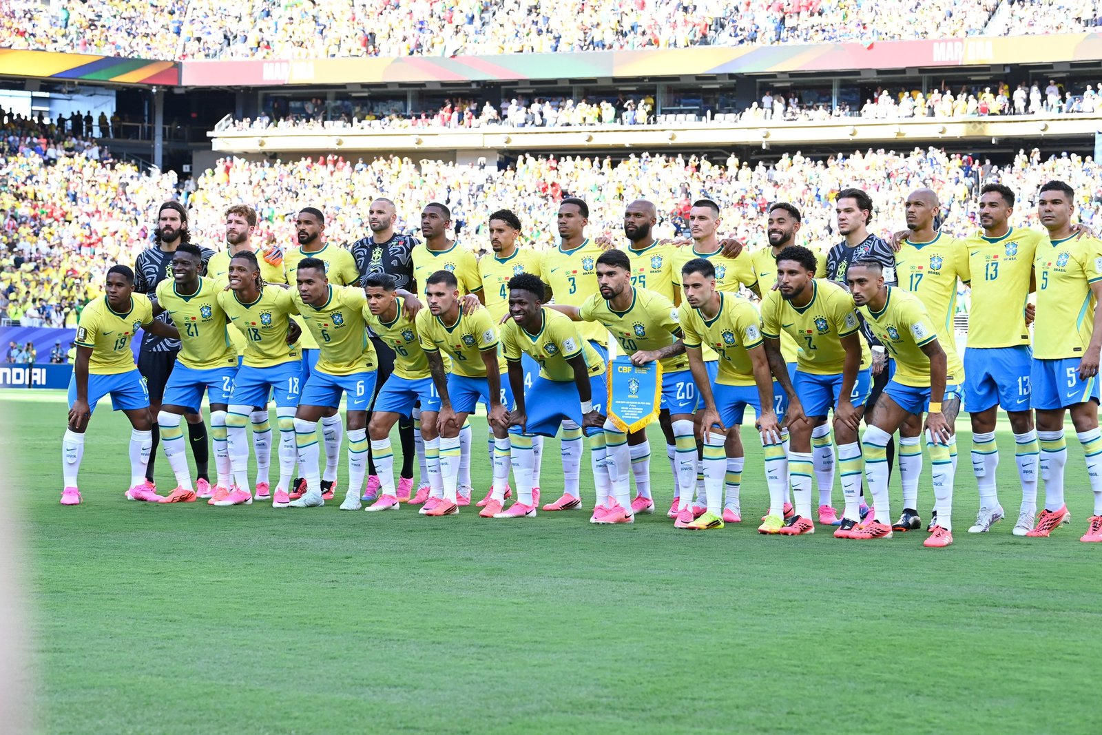 Jogadores da seleção brasileira perfilados no gramado antes de uma partida, de camisa amarela e calção azul
