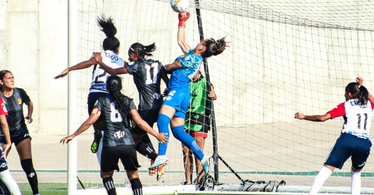 Goleira salta para agarrar a bola no alto durante disputa em partida de futebol feminino