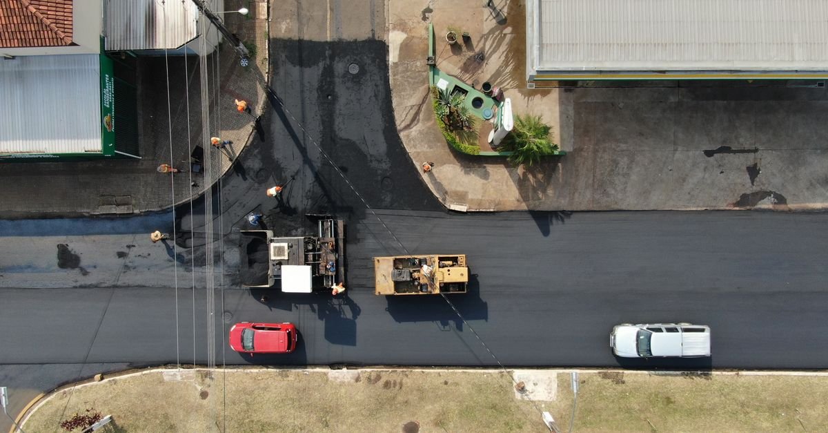 Vista aérea de recapeamento asfáltico em rua com máquinas e equipe de obra