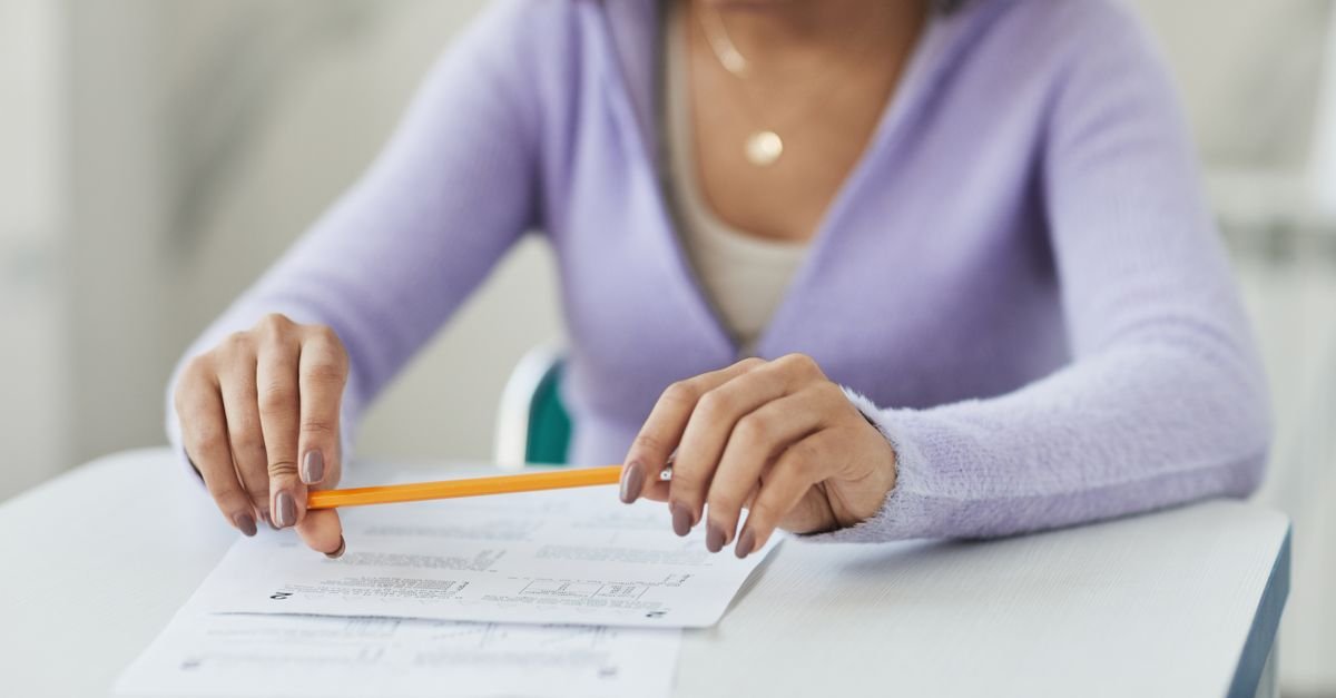 Mãos de uma pessoa segurando um lápis sobre uma prova em papel