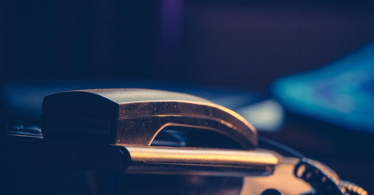 Fone de telefone fixo em close, apoiado no aparelho, sob luz baixa