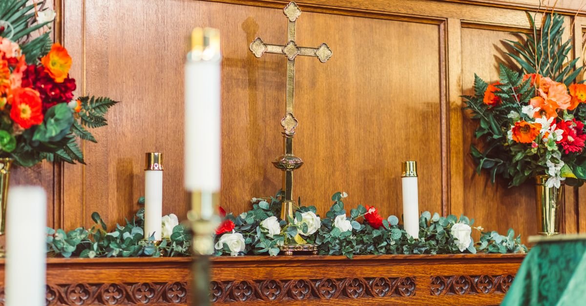 Altar de igreja com velas acesas, flores e uma cruz de madeira