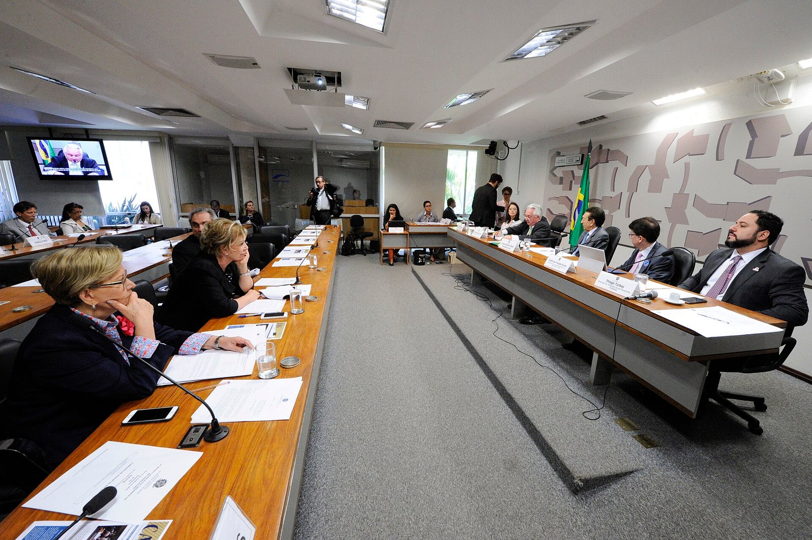 Sala de reuniões da Comissão de Assuntos Sociais do Senado, com senadores às bancadas e a bandeira do Brasil ao fundo