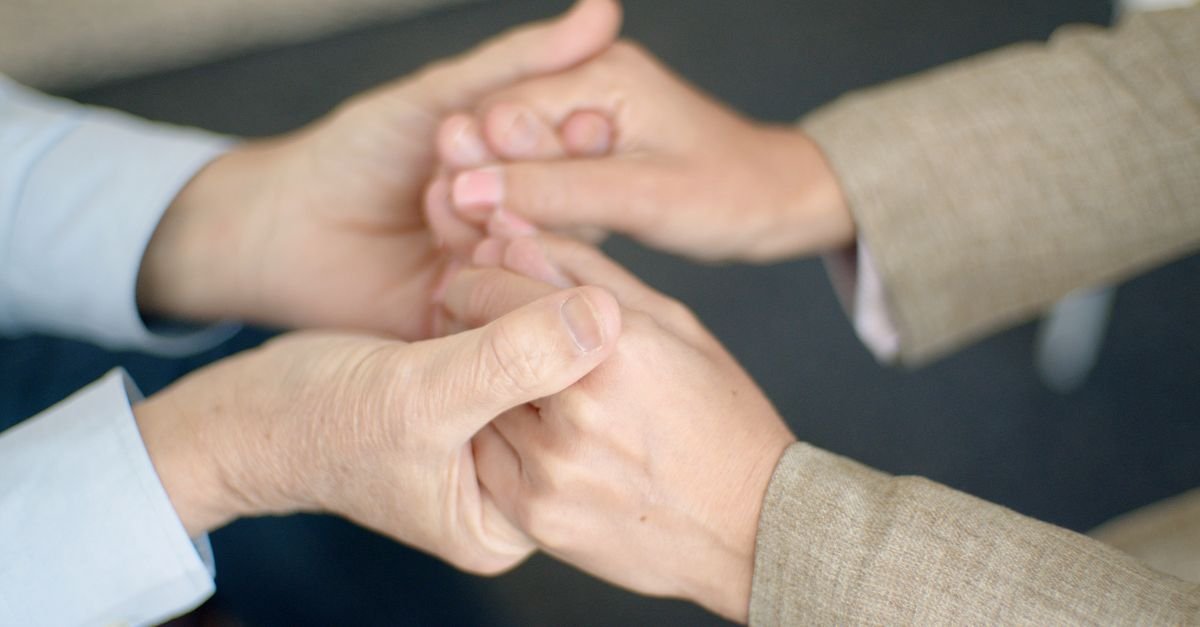 Duas pessoas de mãos dadas em gesto de apoio, em close das mãos