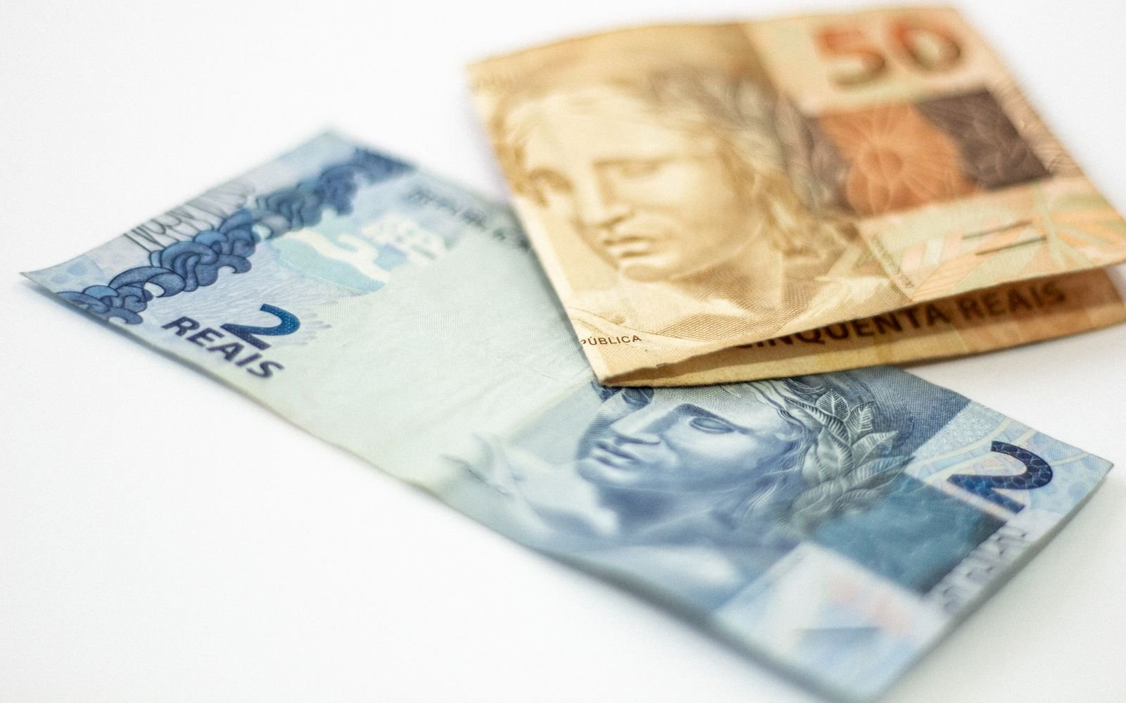 Cédulas de 2 e 50 reais sobre fundo branco