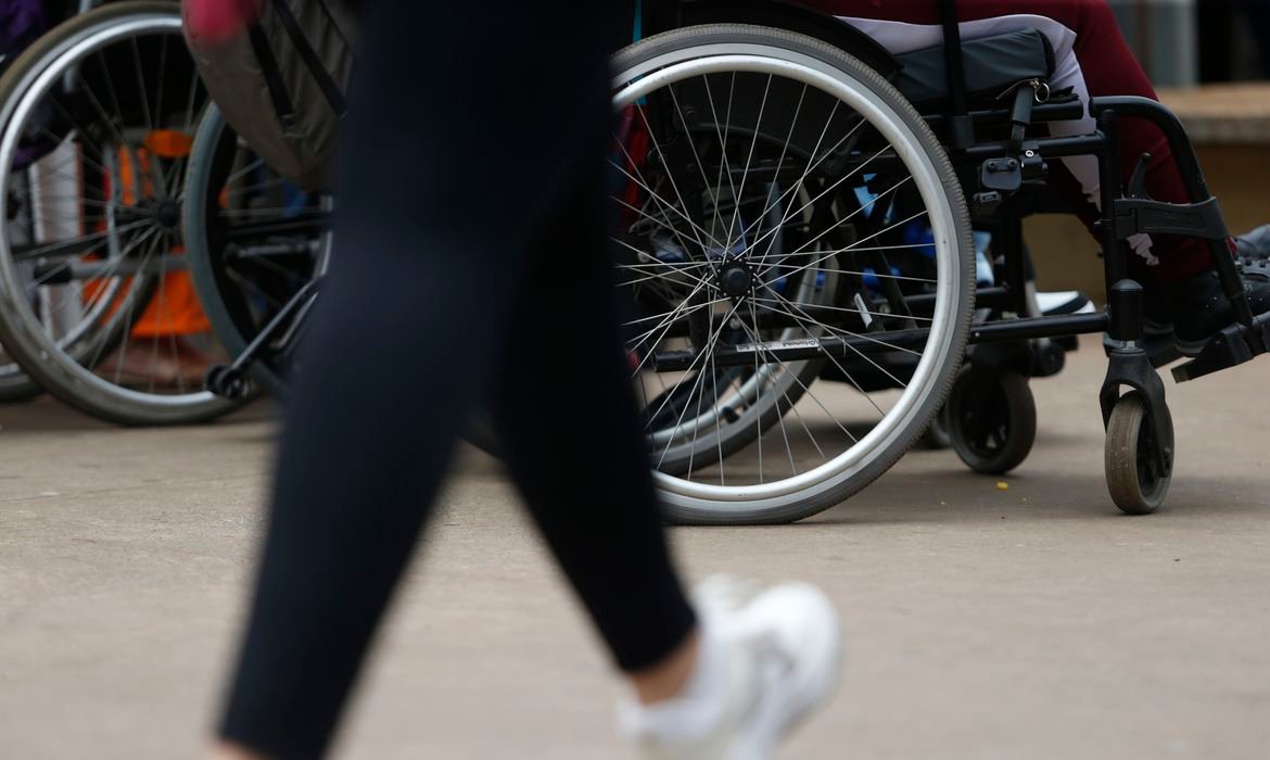 Cadeiras de rodas enfileiradas em calcada enquanto uma pessoa passa caminhando