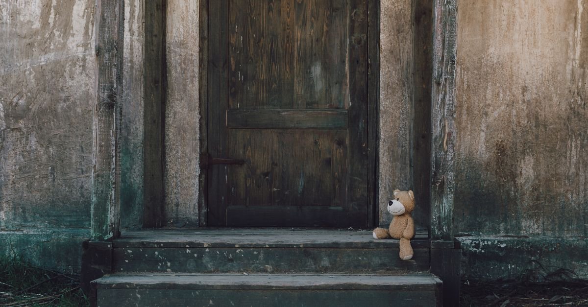 Urso de pelucia abandonado sentado na escada de uma casa antiga