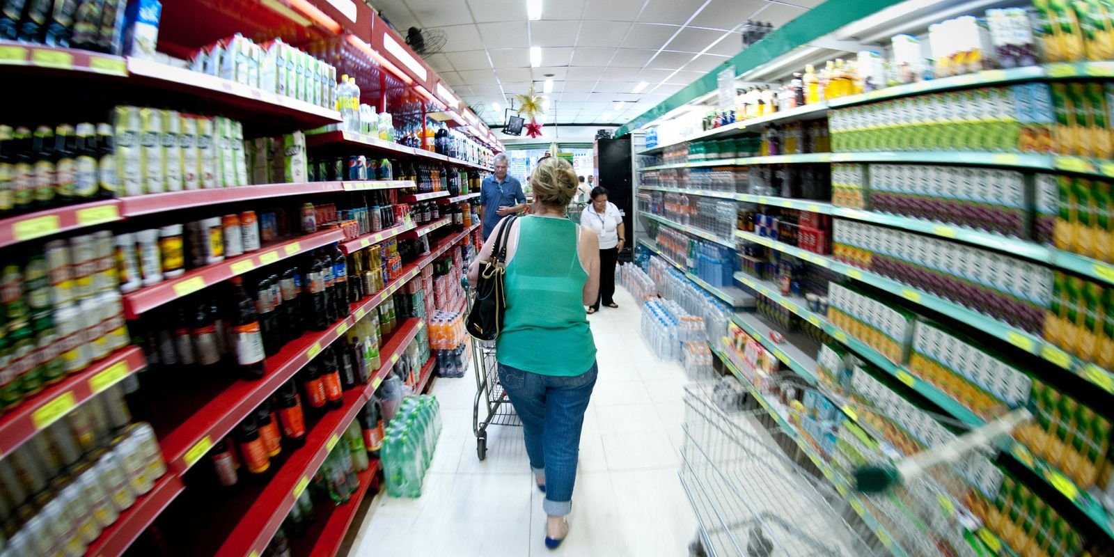 Consumidora empurra carrinho em corredor de supermercado com prateleiras cheias