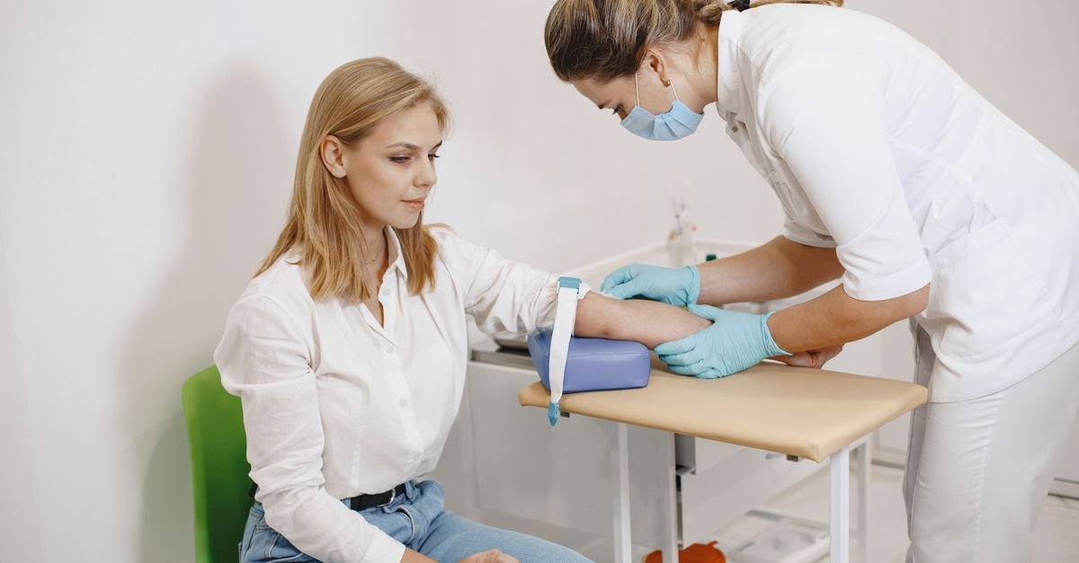 Profissional de saúde coleta sangue do braço de uma paciente sentada em consultório