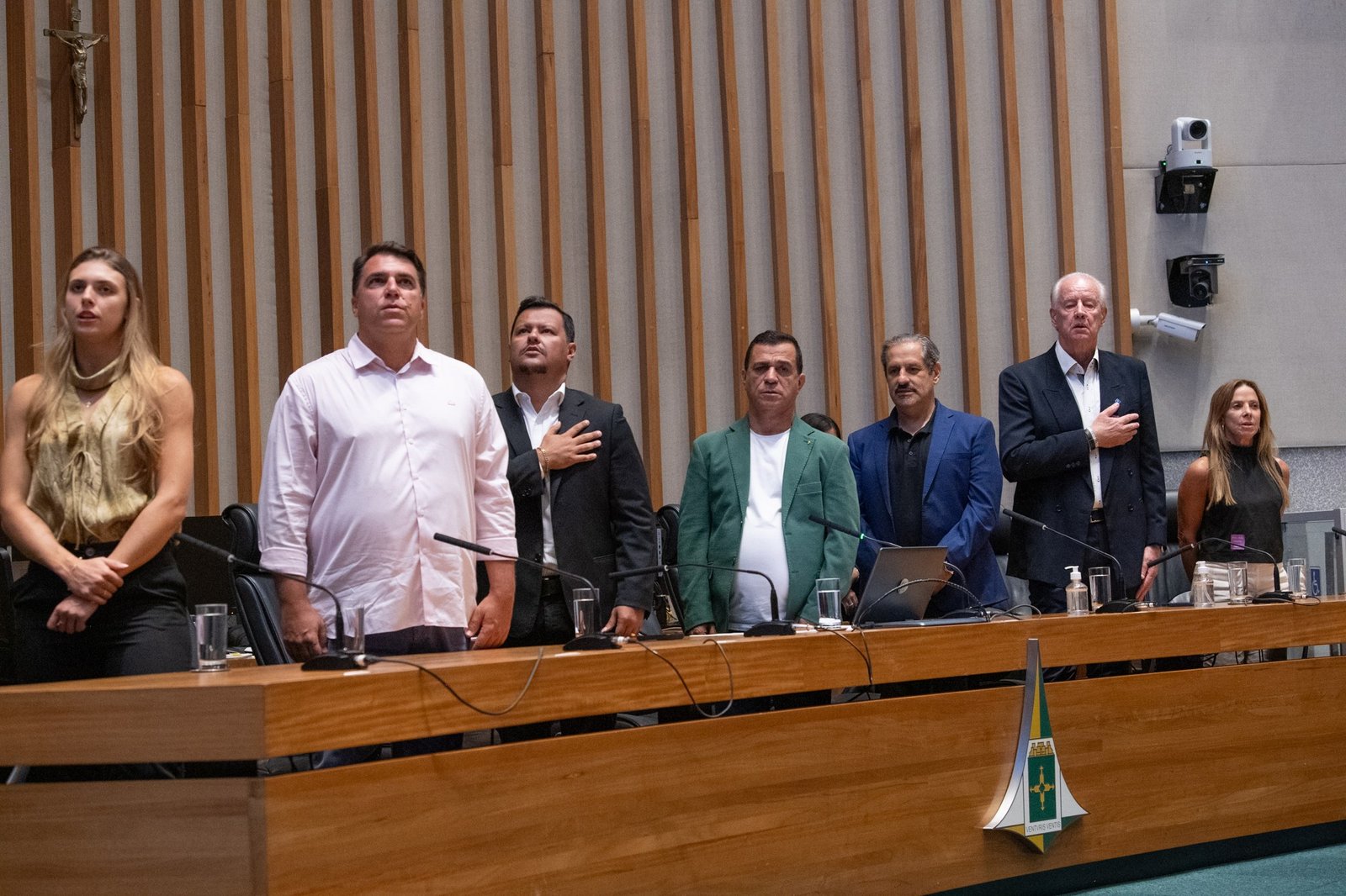 Plenário da Câmara Legislativa do DF, com o brasão do Distrito Federal na frente da mesa e pessoas em pé durante sessão solene
