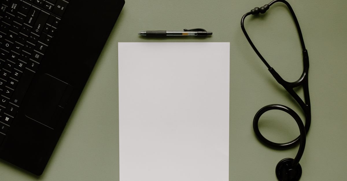 Estetoscópio, folha em branco e computador sobre mesa de consultório