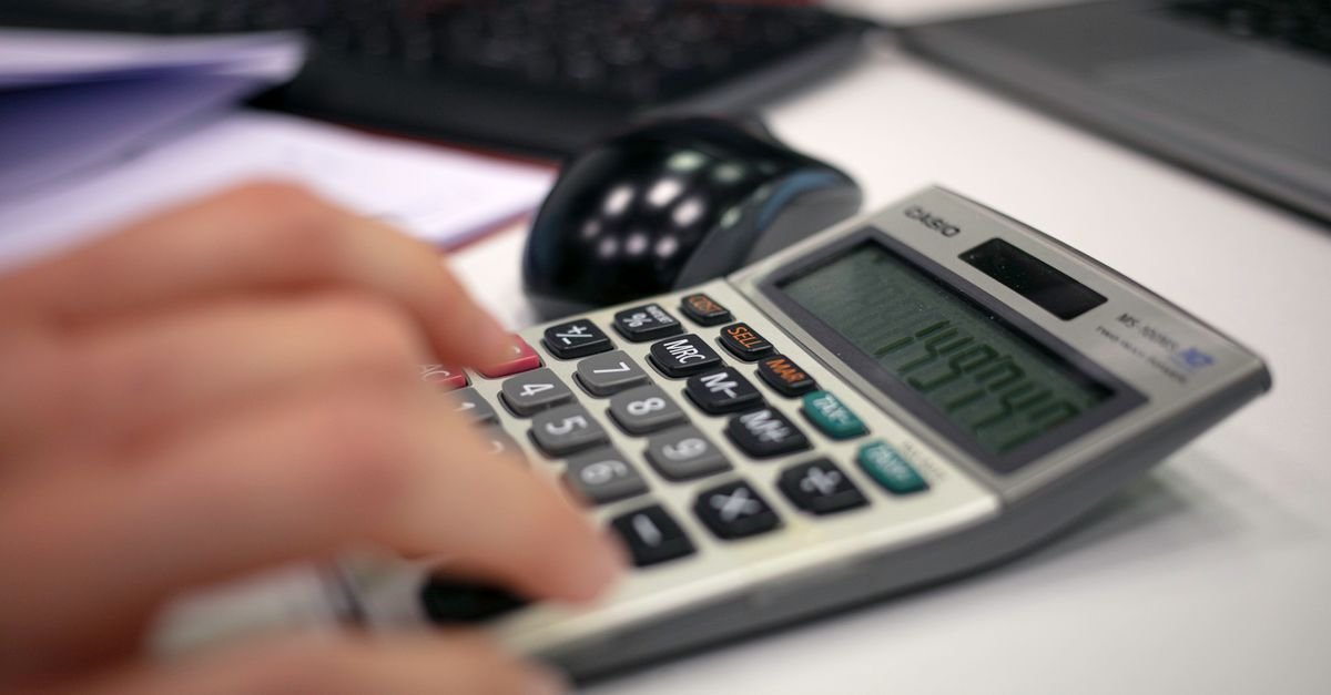 Mão operando calculadora sobre mesa de escritório