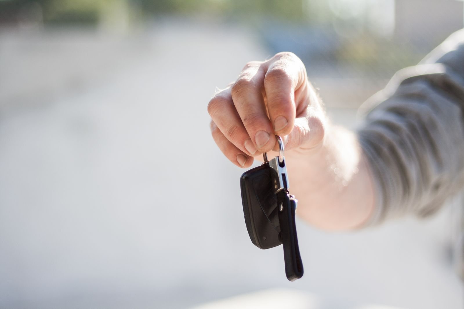 Mão estendida segurando a chave de um carro, com a rua desfocada ao fundo