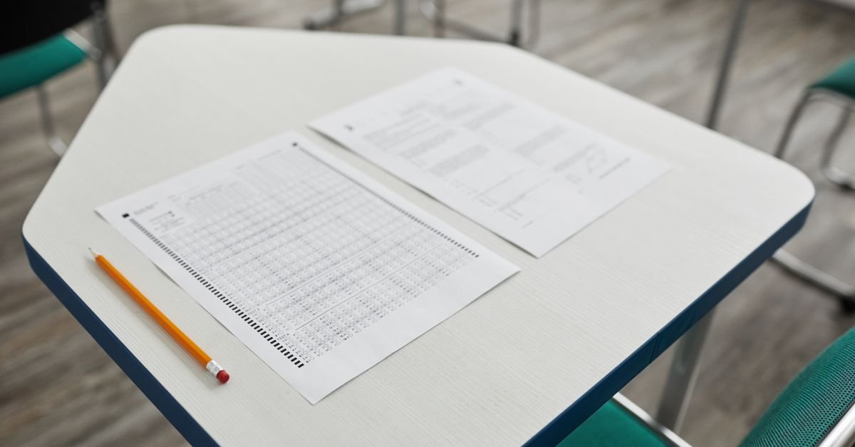Folha de respostas e lápis sobre carteira escolar em sala de prova