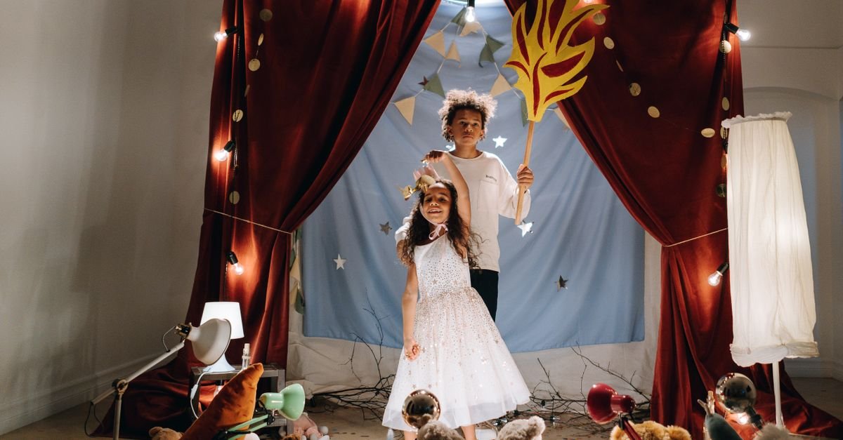 Duas crianças fantasiadas em um palco de teatro com cortinas vermelhas