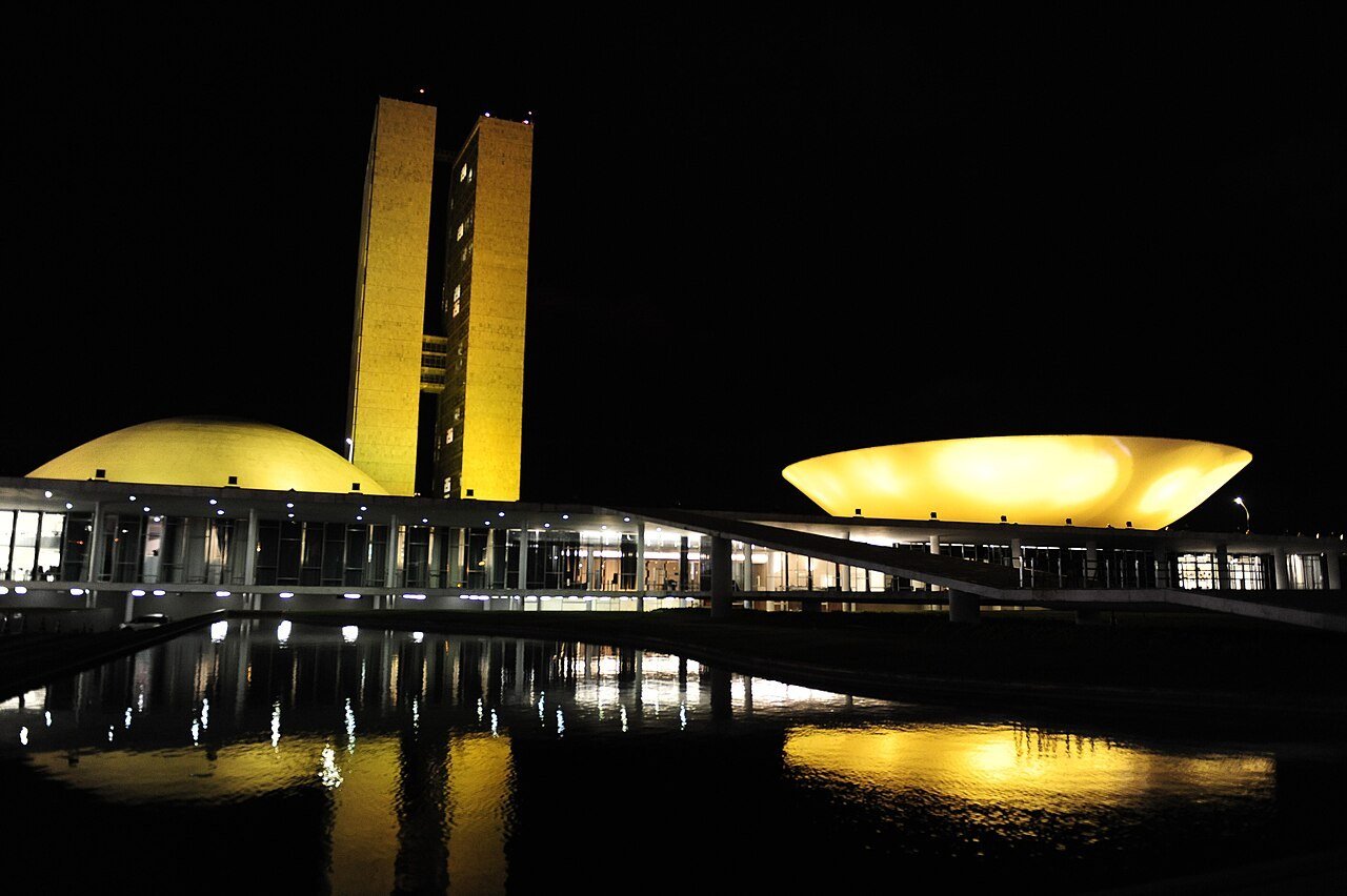 Prédio do Congresso Nacional, em Brasília, iluminado à noite, com as duas torres e as cúpulas refletidas no espelho d'água (foto de arquivo)