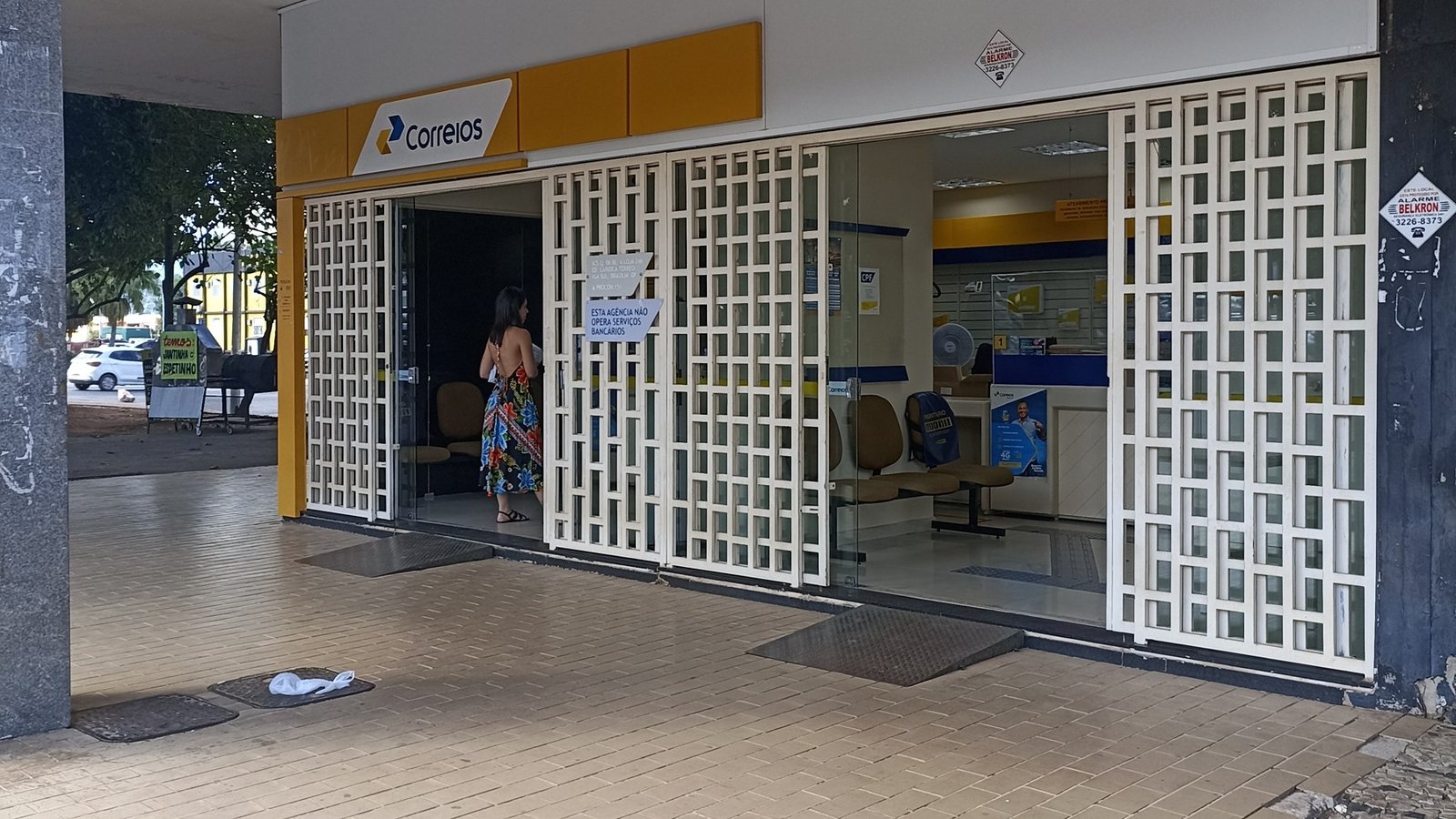 Fachada de agência dos Correios no Setor Comercial Sul, em Brasília, com porta gradeada e cliente entrando