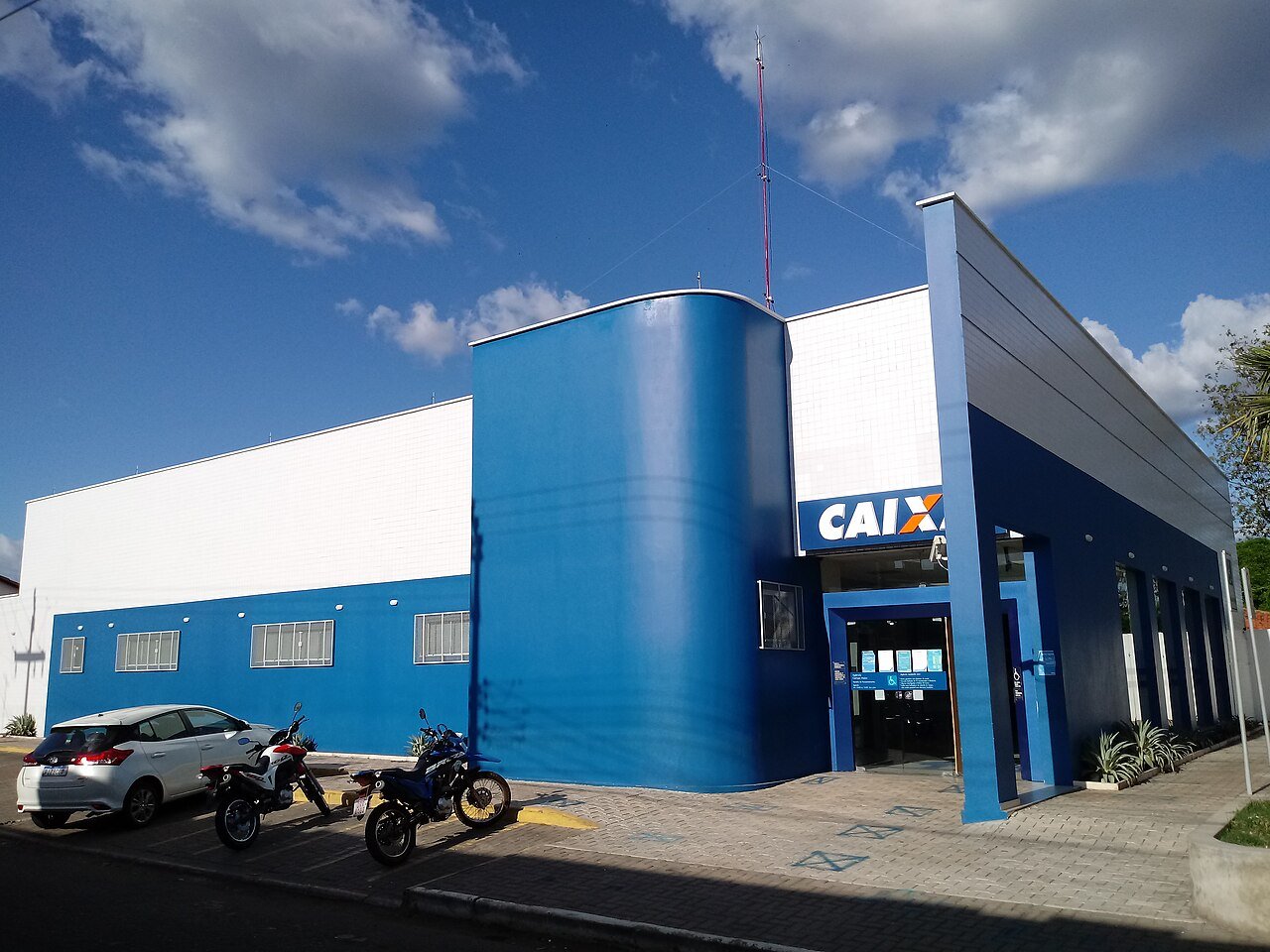 Fachada de uma agência da Caixa Econômica Federal, com o letreiro azul e laranja sobre a entrada