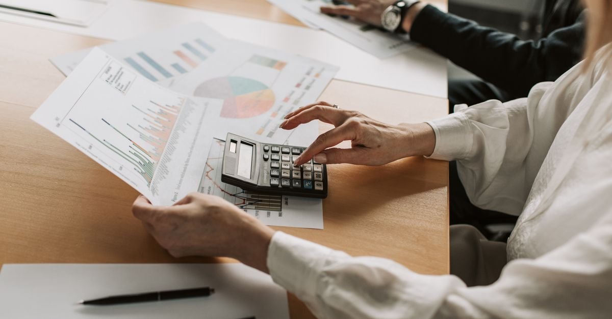 Mãos analisam gráficos financeiros impressos com calculadora sobre mesa de reunião
