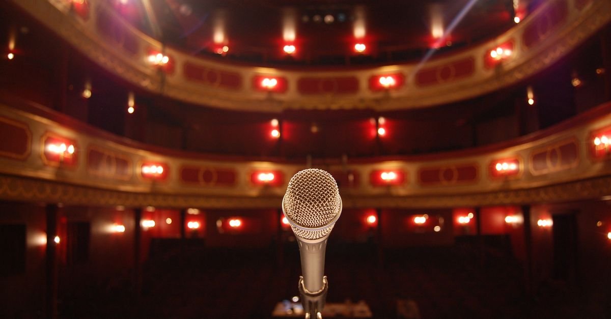 Microfone em primeiro plano no palco de um teatro com plateia ao fundo