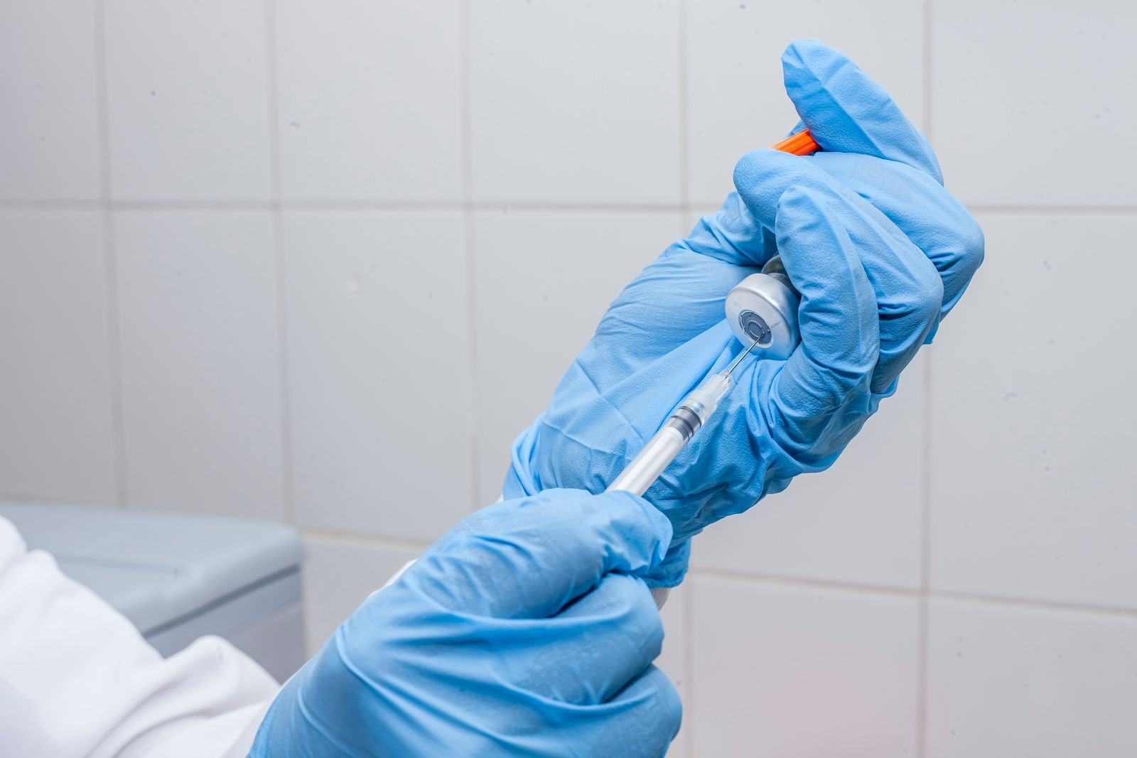 Mãos com luvas azuis preparam uma seringa com dose de vacina de um frasco, em foto ilustrativa