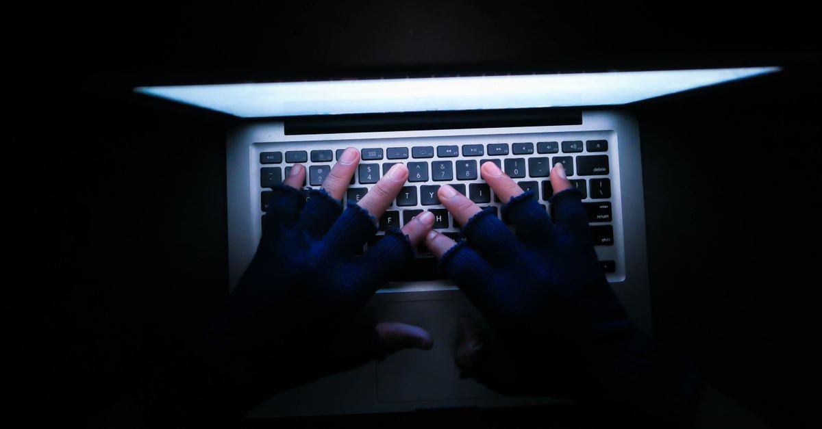 Mãos com luvas sem dedos digitando em teclado de notebook em ambiente escuro