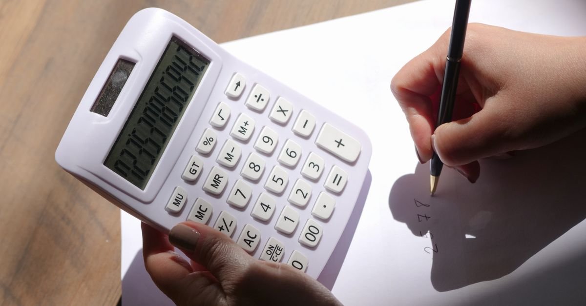 Mãos de uma pessoa segurando uma calculadora e anotando valores em uma folha de papel