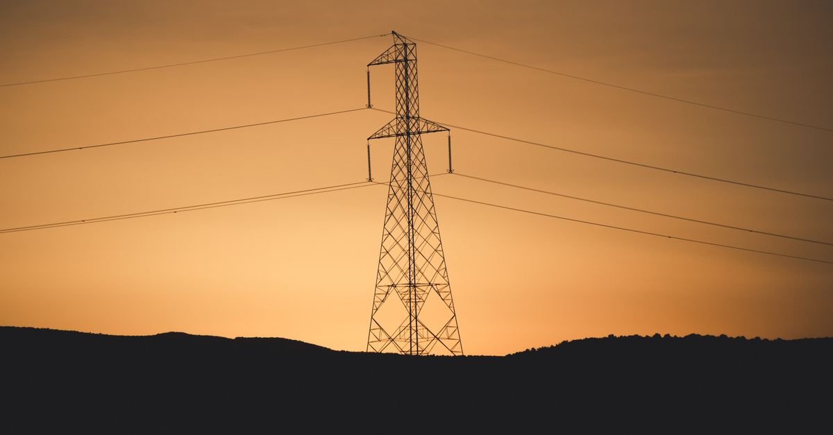 Silhueta de torre de transmissão de energia elétrica com cabos ao entardecer