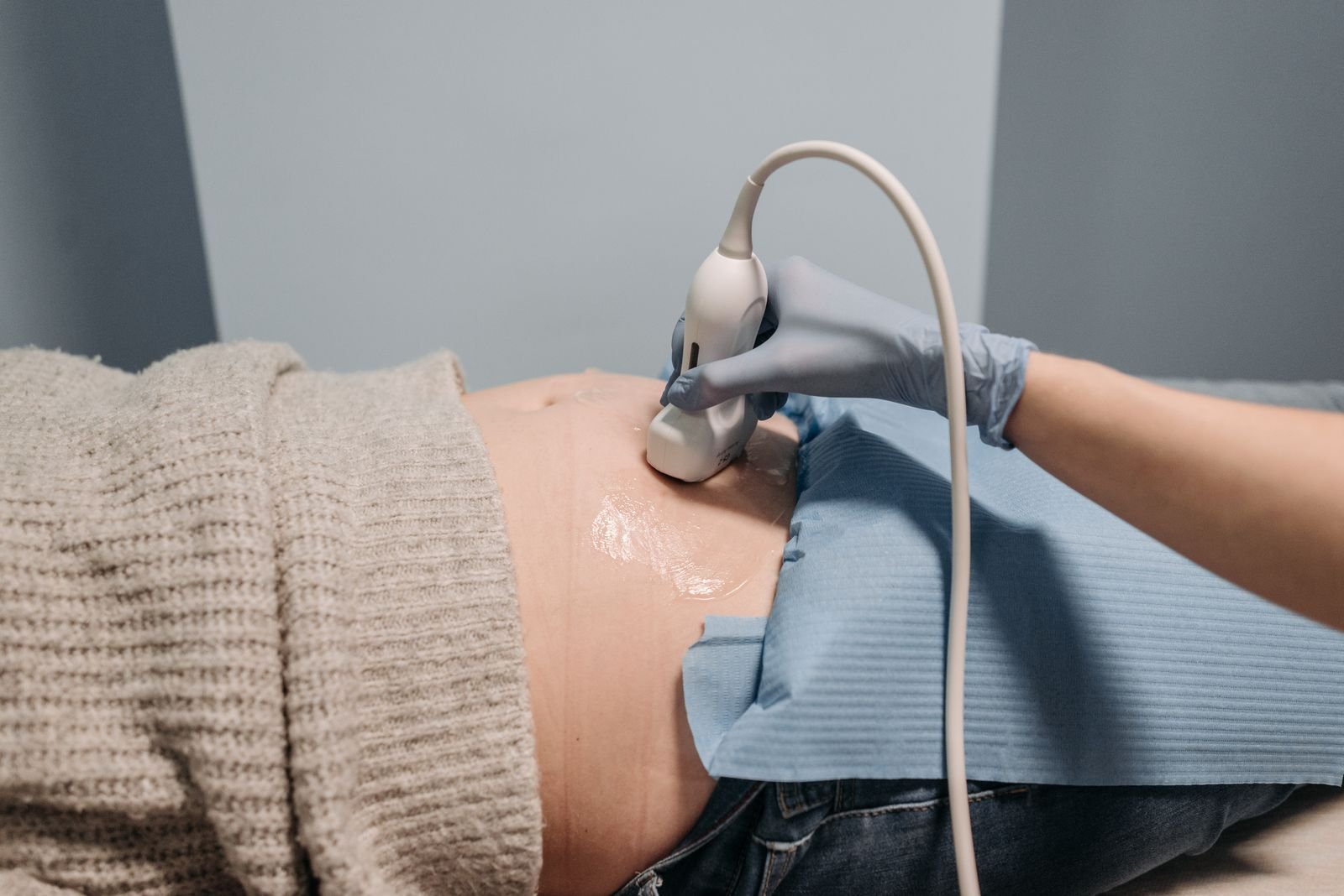 Profissional de luvas faz ultrassom no abdome de uma gestante em consultório