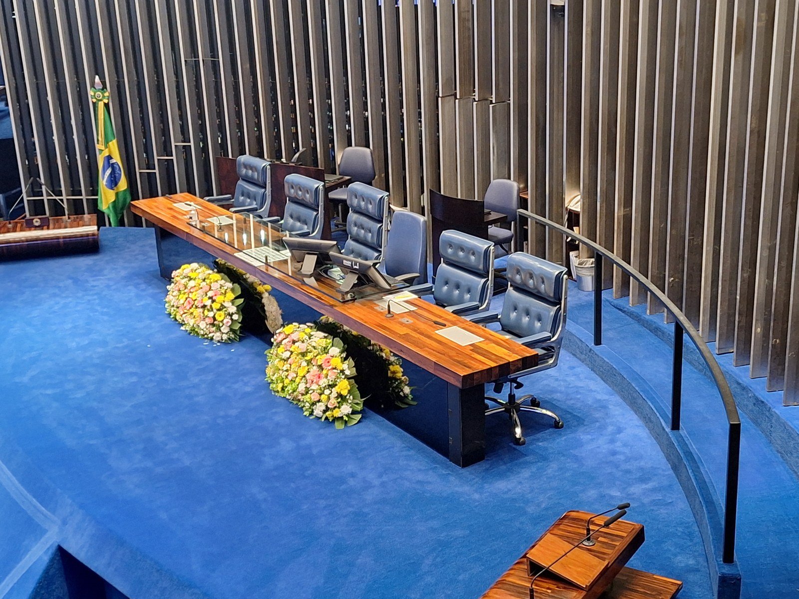 Mesa diretora do plenário do Senado Federal, com cadeiras azuis e arranjos de flores