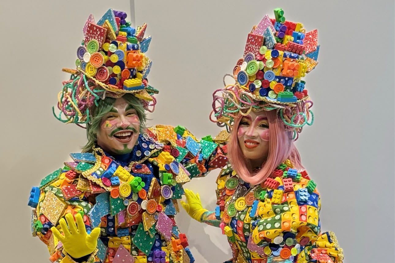 Dois personagens com fantasias e chapéus cobertos de peças coloridas de brinquedo, em imagem de divulgação do Pontão do Lago Sul