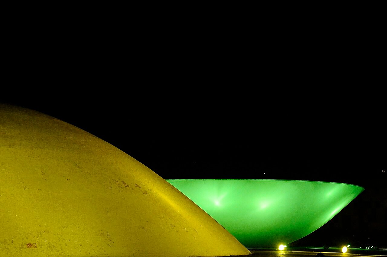 Cúpulas do Congresso Nacional iluminadas de verde e amarelo à noite, em Brasília
