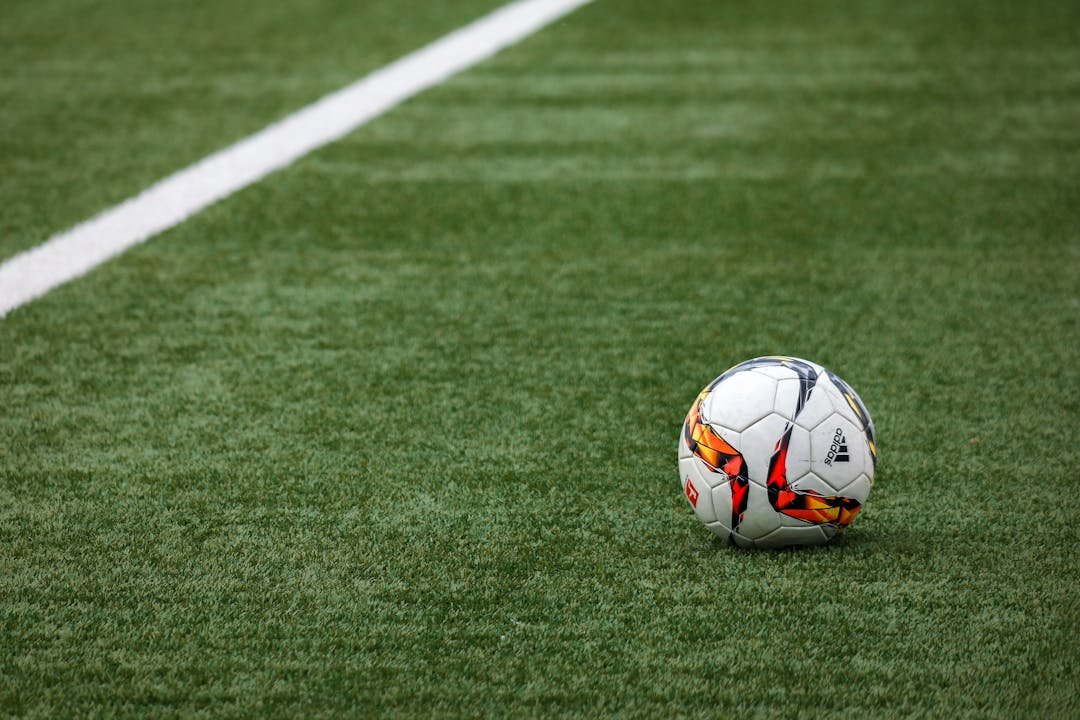 Bola de futebol oficial parada em campo de grama com linha branca lateral