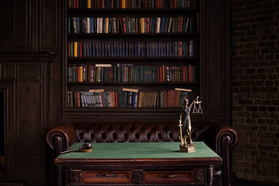 Sala de estudo com estatua da Justica gavel sobre mesa e estante de livros juridicos