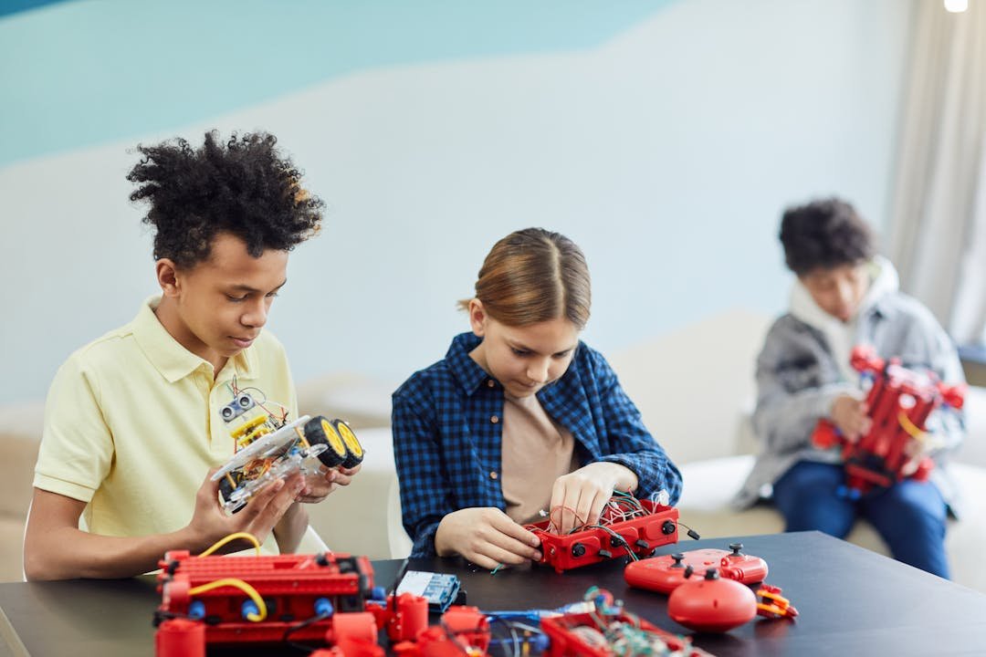 Adolescentes manipulando kits de robotica vermelhos em mesa