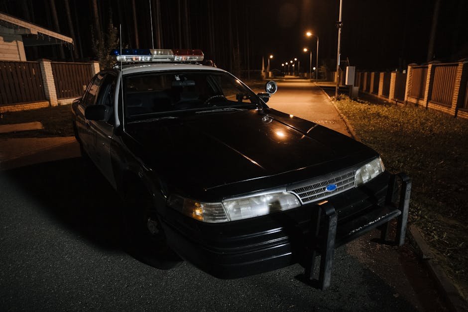 Viatura policial preta com luzes giroflex em rua à noite