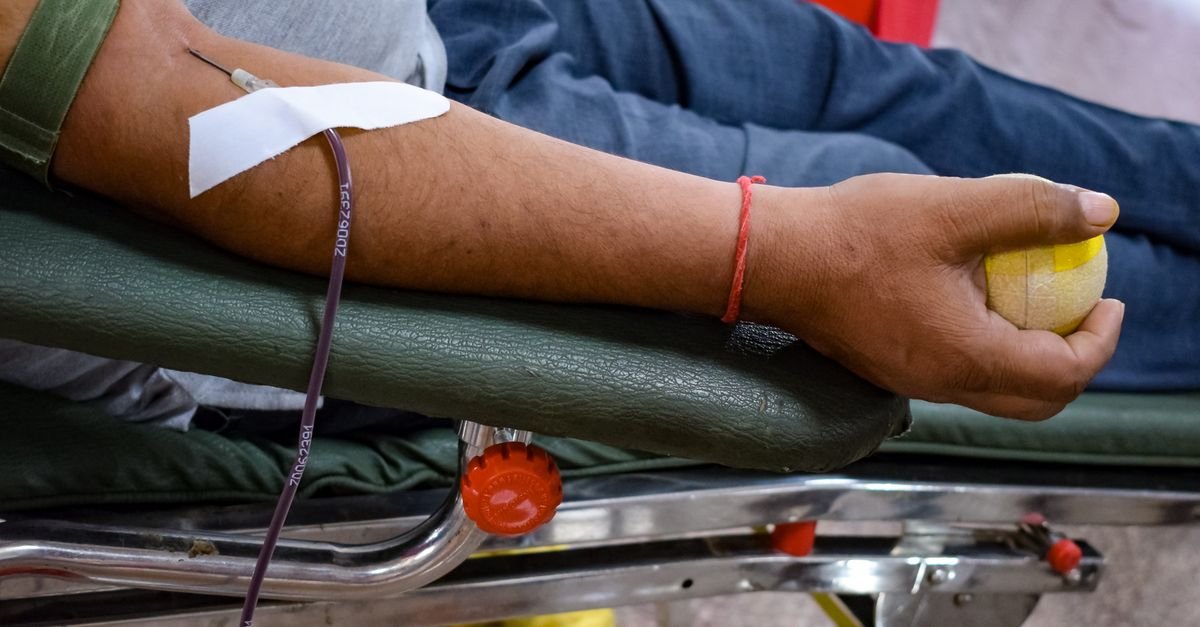 Braço de doador com agulha e esparadrapo durante coleta de sangue em cadeira de hemocentro