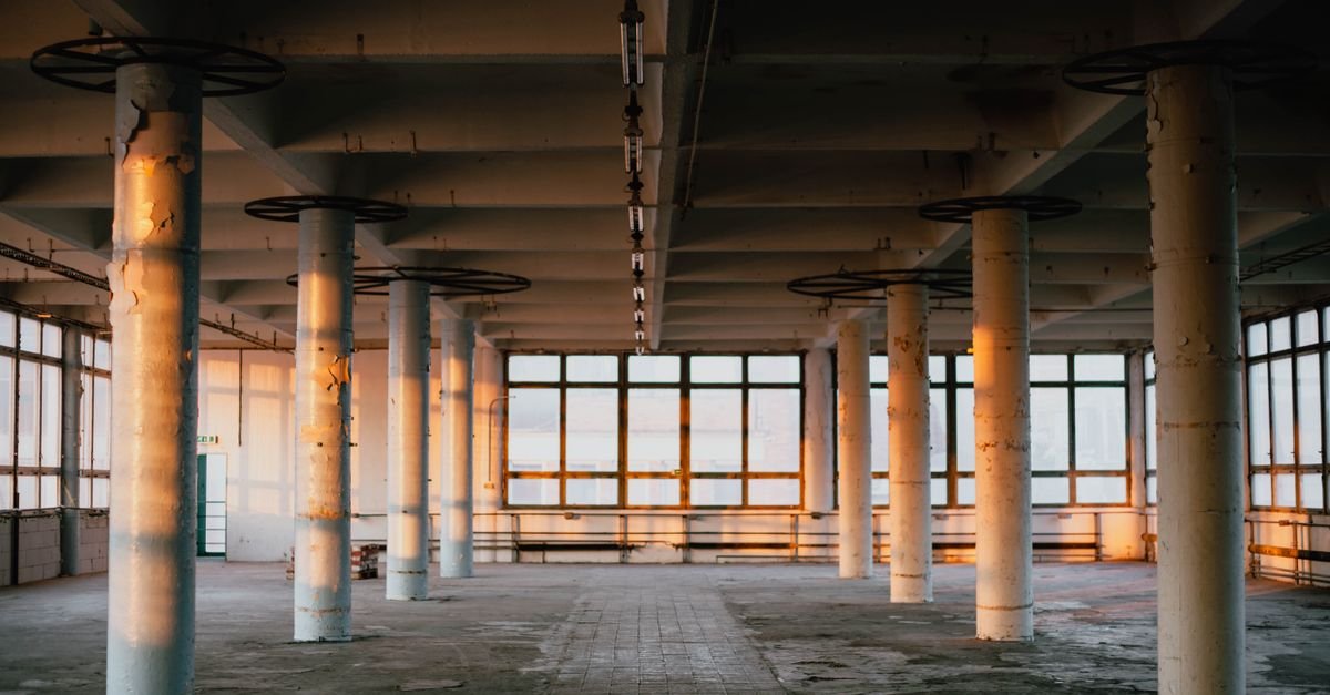 Interior vazio de galpão industrial com colunas de concreto e janelas amplas