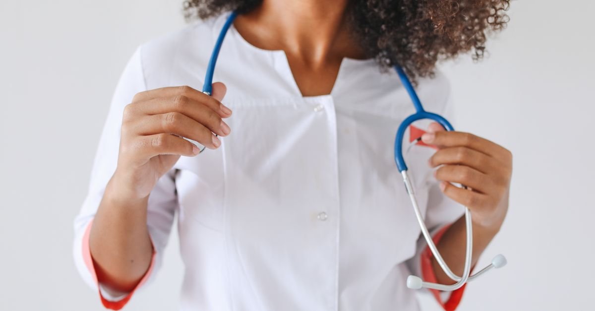 Profissional de jaleco branco segura um estetoscópio azul diante do corpo, sem o rosto à mostra