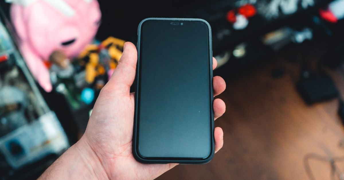 Mão segurando um celular com a tela apagada em ambiente interno