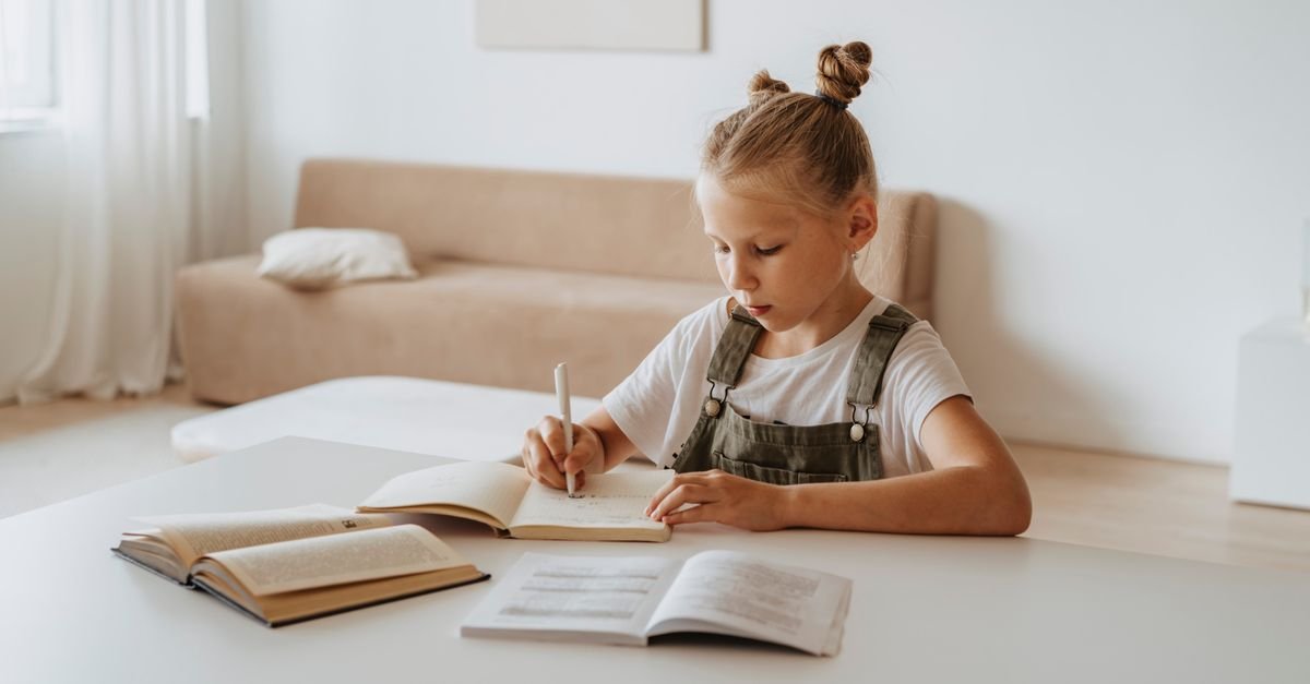 Criança estuda em casa com livros e caderno sobre a mesa