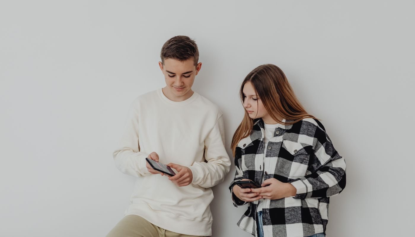 Adolescentes usando smartphones encostados em parede clara